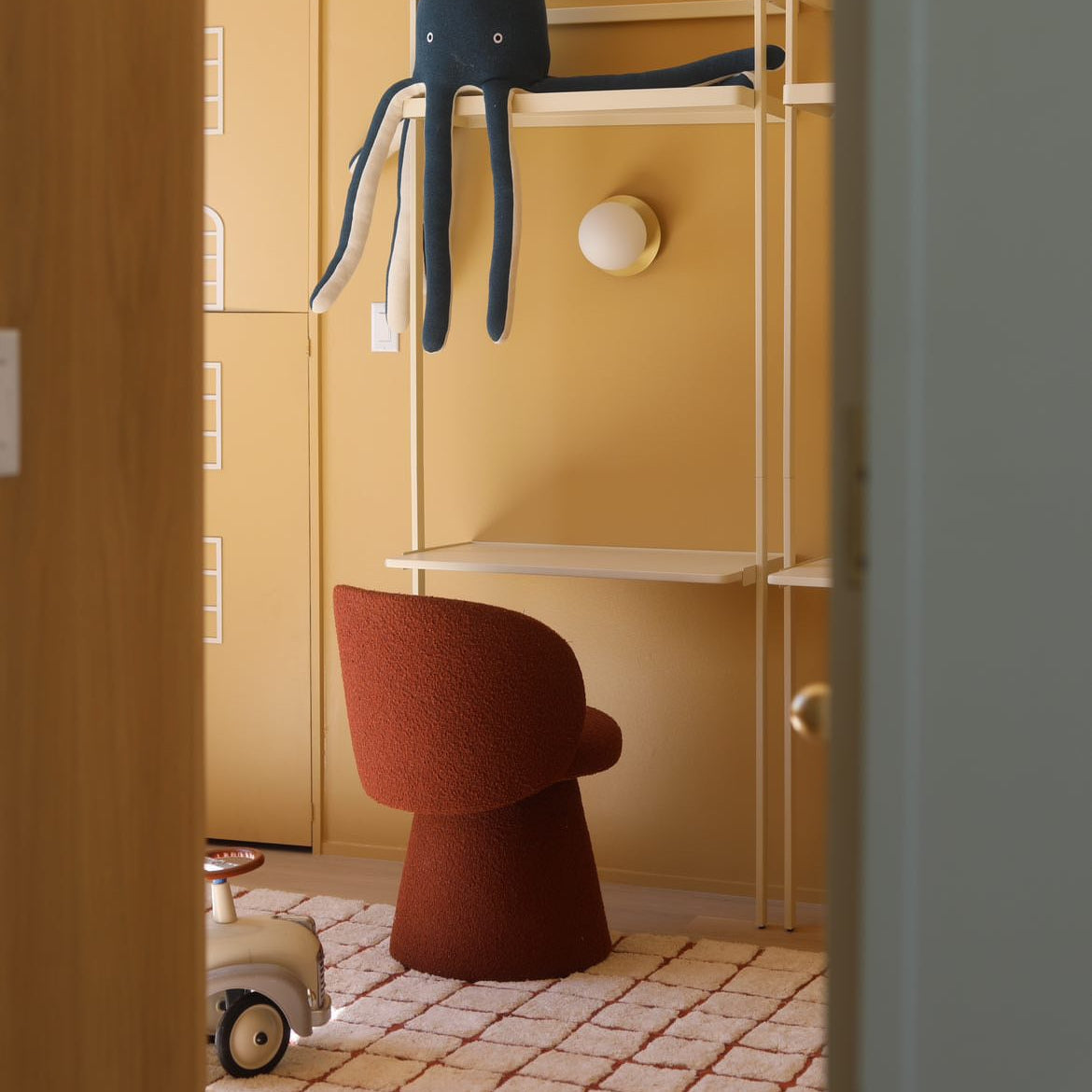 Nursery with a blue elephant toy on a shelf, a red chair, and a yellow wall.