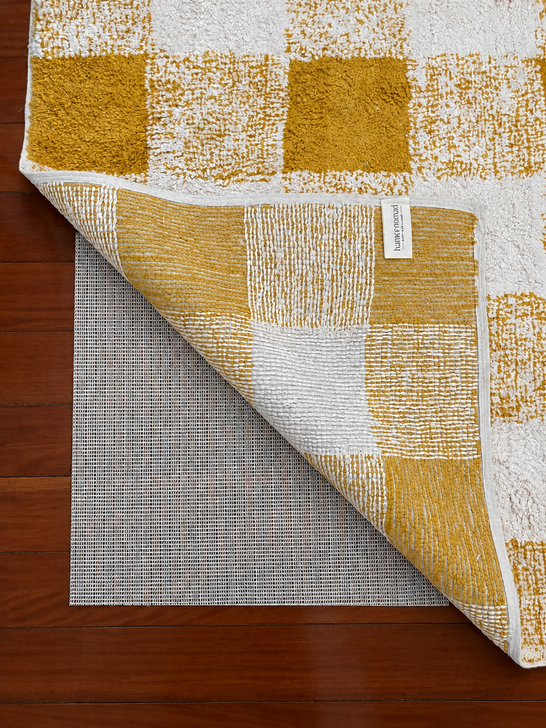 Non-slip rubber rug underlay beneath a folded mustard gingham cotton rug